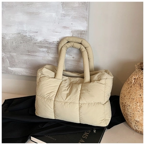 Detail van beige gewatteerde puffer tote bag geplaatst op donkere kleding in artistieke setting