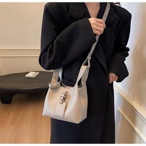 Détail du sac seau en cuir grainé gris clair avec boucle métallique porté par un mannequin