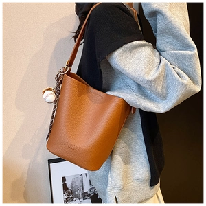 Detail of a brown lychee pattern bucket bag with a baseball charm and silk scarf