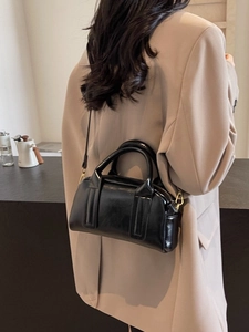 Glänzende schwarze Boston-Tasche auf der Schulter einer Frau im khakifarbenen Blazer