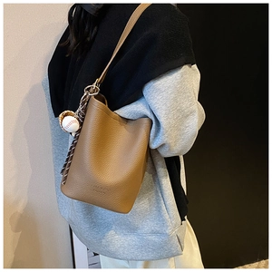 Detail view of brown lychee grain leather bucket bag with baseball charm and brand logo