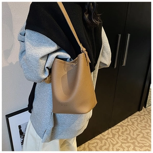 Detail showing the brown litchi grain leather texture and shoulder strap on a bucket bag