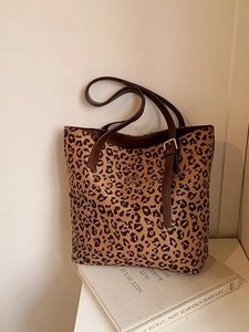 Leopard print tote bag with brown leather straps displayed on a book in a cozy setting