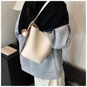 Detail of off-white lychee pattern leather bucket bag with baseball charm on model