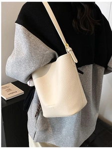 Minimalist beige pebble leather bucket bag featuring adjustable shoulder strap and logo detail