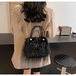 Detail of black faux fur mini bag with pearl accent and gold chain strap on a model