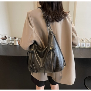 Detail of black leather hobo bag featuring decorative zippers and leather bow accents