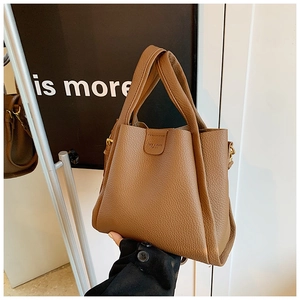 Detail of brown litchi pattern leather bucket bag held by a model in a chic studio