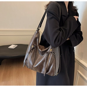 Close-up of brown PU leather tote bag featuring double zippers and bow drawstring details