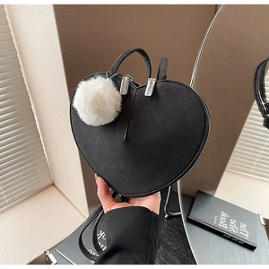 Détail du sac à main noir en forme de cœur avec pompon blanc et finitions en métal argenté