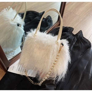 Detail of white faux fur bucket bag with pearl gold chain and leather handle on black silk