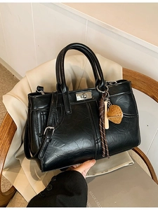 Sac à main noir classique avec boucle argentée et charm fraise sur un fauteuil chic