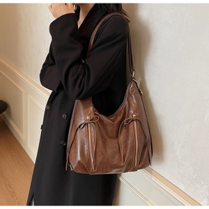 Detail of dark brown hobo shoulder bag featuring stylish side zippers and leather bows