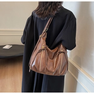 Close-up of brown leather hobo bag featuring decorative zippers and bow tie details