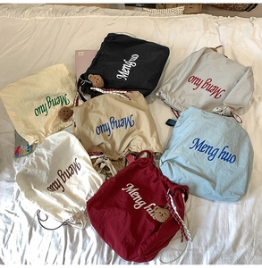 Flat lay of colorful nylon drawstring tote bags in seven colors on a white fabric surface