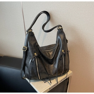 Detail of black textured leather hobo bag with vintage gold zippers and long tassels