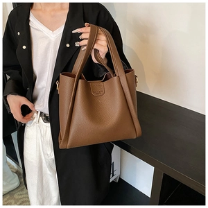 Detail of dark brown leather tote bag showing grainy texture and embossed metal buckle
