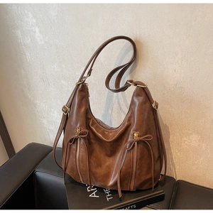 Detail of dark brown leather tote bag with decorative bow zippers on a vintage sofa