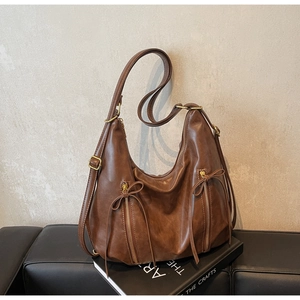 Detailed shot of a vintage brown crescent bag with vertical bow zippers on a leather sofa