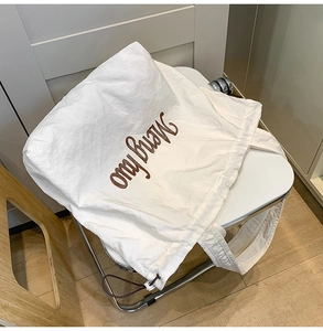 Detail of white nylon tote bag featuring brown embroidered lettering and drawstring