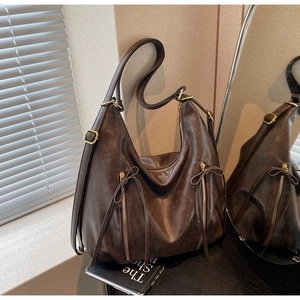 Detail of dark brown leather hobo bag with side zippers and decorative bows