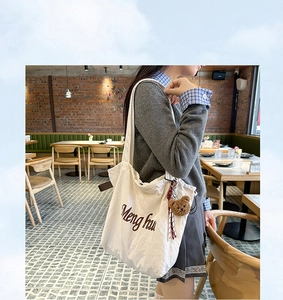 Detailed shot of white canvas tote bag with brown embroidery and plush bear charm