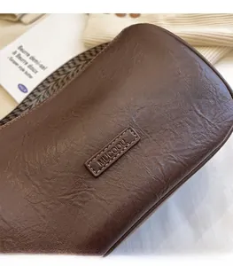 Detail of dark brown leather pillow bag with MUCOOU embossed logo and houndstooth strap