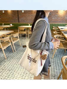 Close-up of white canvas tote bag with brown embroidery and plush bear charm