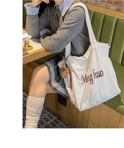 Close-up of white canvas tote bag featuring brown script print and plush bear charm