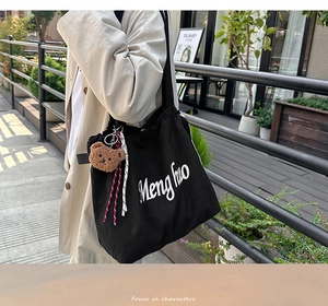 Detail of black canvas tote bag with white cursive text and brown plush bear charm