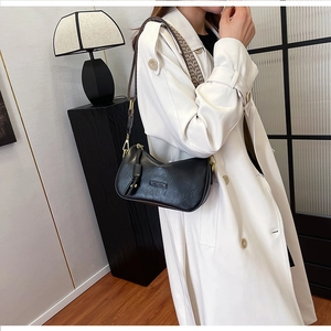 Detail of black leather crescent bag with gold hardware and woven strap on a white coat