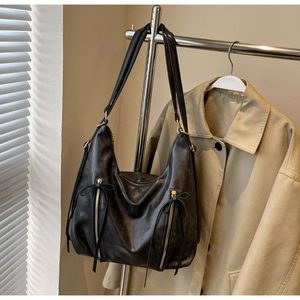 Detail of black leather tote bag featuring ribbon zipper pulls and dual shoulder straps