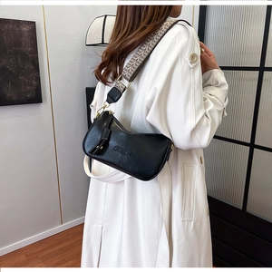 Detail of black leather half-moon bag featuring woven shoulder strap and embossed logo