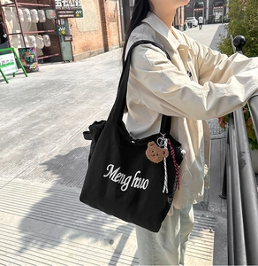 Close-up of black canvas tote bag with white script print and cute plush bear charm