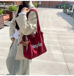 Close-up of wine red canvas tote with Menghuo embroidery and a cute bear keychain