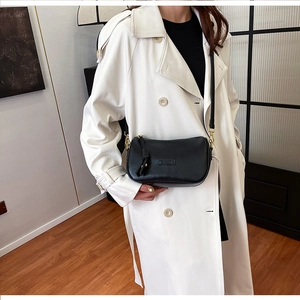 Detail of a black leather pillow bag with gold buckles worn with a white trench coat