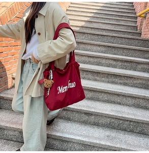 Detail of red canvas tote bag featuring Menhuo logo and a cute brown plush bear charm