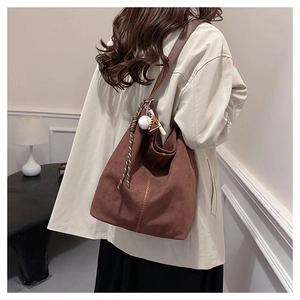 Detailansicht einer dunkelbraunen Wildleder-Hobo-Tasche mit Baseball-Anhänger und Kordel