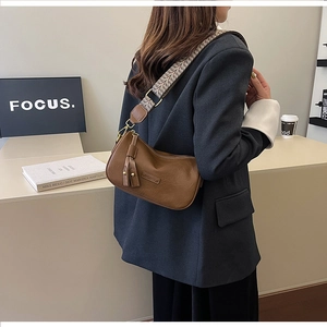 Brown leather crossbody bag with checkered strap and tassel detail in a lifestyle setting