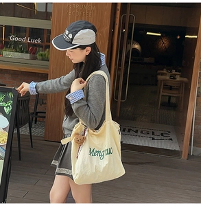 Outdoor shot of a cream canvas tote bag with green lettering and a cute bear charm