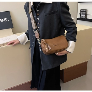 Detail of brown leather crossbody bag with wide patterned strap on a stylish model