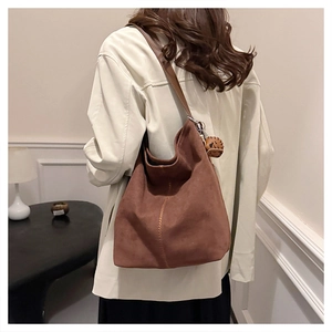 Detail einer braunen Wildleder-Hobo-Tasche mit vertikaler Naht und Anhänger am Schultergurt