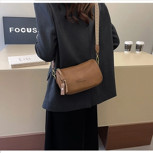 Detailed view of a vintage brown crossbody bag featuring wide woven strap and fringe tassel
