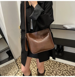 Sac bandoulière marron vintage en similicuir porté par un mannequin dans un salon