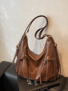 Retro deep brown leather tote bag with stylish bow zipper pulls on a studio background