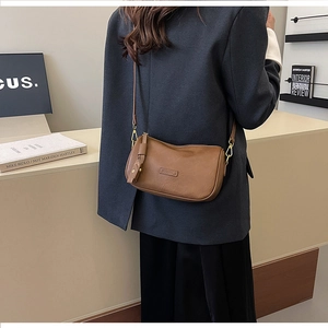 Detail of caramel leather crossbody bag with tassel charm and adjustable strap shown on model
