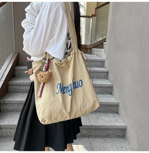 Detail of beige canvas tote bag with drawstring closure and cute plush bear charm