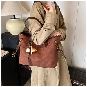 Détail du cabas en daim marron avec un porte-clés baseball créatif et une poignée en cuir