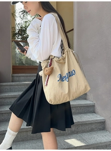 Detail of beige tote bag with blue Mengnuo logo, plush bear charm and ribbon decor