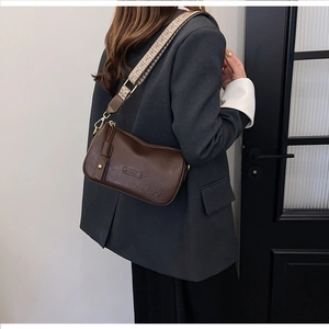 Detail of dark brown retro pillow bag with ethnic wide strap on a grey suit jacket